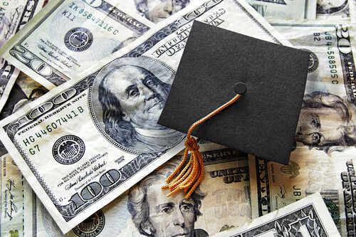Miniature,Graduation,Cap,On,Hundred,Dollar,Bills A graduation cap placed on a pile of U.S. dollar bills