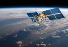 A satellite equipped with solar panels orbiting above the Earth, surrounded by clouds