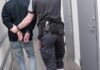 Security officer escorts handcuffed person down hallway