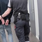 Viral Tale Unravels: Records Tell Another Security officer escorts handcuffed person down hallway