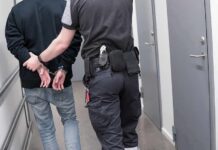 Security officer escorts handcuffed person down hallway