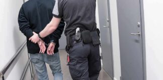 Security officer escorts handcuffed person down hallway