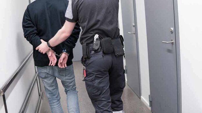 Security officer escorts handcuffed person down hallway