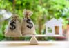 Money bags and house cutout on a balance scale