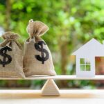 Homeownership Keeps Moving Out Of Reach Money bags and house cutout on a balance scale