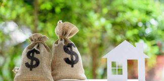 Money bags and house cutout on a balance scale
