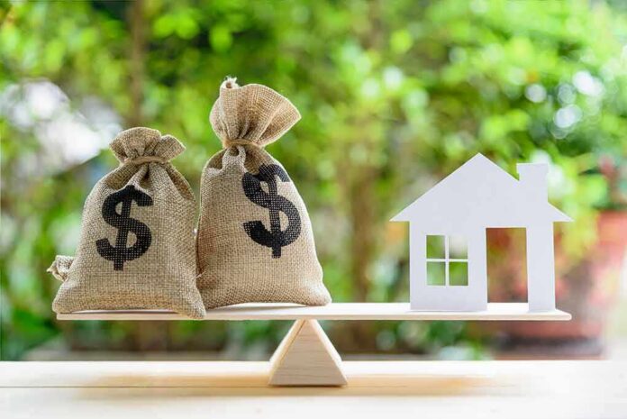 Money bags and house cutout on a balance scale