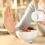 Eating Late Could Cost More Than Sleep Person holding an alarm clock with a bowl of cereal in front
