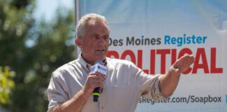 Man speaking on an outdoor stage with a microphone
