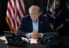 Trump Escalates Warning Against Tehran A serious-looking man seated at a table with phones and an American flag in the background