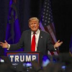 Trump’s Collins Joke Sparked a New Culture Clash speaker at podium with flags addressing audience