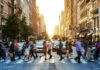People crossing a busy city street at sunset