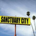 Sanctuary Shields, Three Dead — Who Stopped ICE? Yellow roadside sign reading Sanctuary City with palm trees