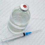 Vial of clear liquid with syringe on a white surface
