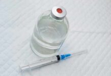 Vial of clear liquid with syringe on a white surface
