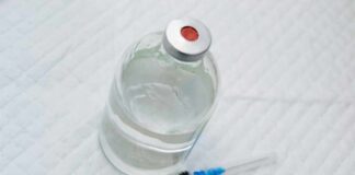 Vial of clear liquid with syringe on a white surface