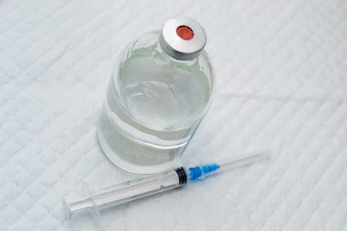 shutterstock_1352442560 Vial of clear liquid with syringe on a white surface