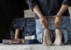 Person in handcuffs kneeling beside an open suitcase with cash
