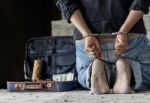 Person in handcuffs kneeling beside an open suitcase with cash