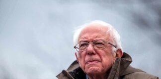 elderly man in glasses speaking outdoors into microphones