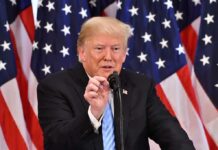 Donald Trump speaking at a podium with American flags in the background