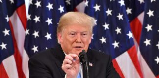 Donald Trump speaking at a podium with American flags in the background