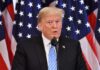 man speaking at podium with American flags behind