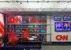 CNN Number-Cruncher Sounds Blue Bias Alarm CNN newsroom set with red chairs and multiple TVs