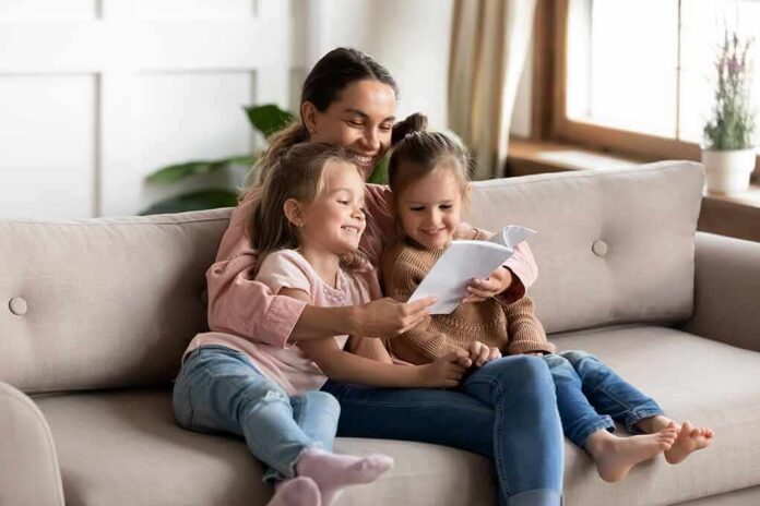 Woman reading a book with two young girls on a sofa