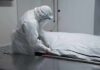 Healthcare worker in PPE zipping a body bag on a gurney