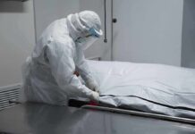 Healthcare worker in PPE zipping a body bag on a gurney