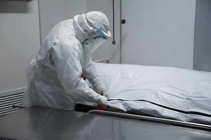 Healthcare worker in PPE zipping a body bag on a gurney