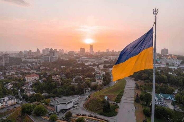 shutterstock_2094921034 Ukrainian flag flying over a city at sunset