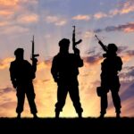 Silhouettes of three armed soldiers at sunset