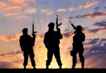 Silhouettes of three armed soldiers at sunset