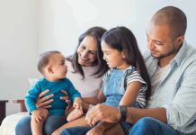 Family sitting on couch with parents, daughter, and baby smiling together