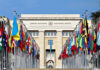 UN Shock Play: Orbán Backed by Three Giants? United Nations building with numerous national flags outside.
