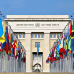 UN Shock Play: Orbán Backed by Three Giants? United Nations building with numerous national flags outside.