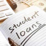 Notebook with student loans written, marker, cash, and keyboard