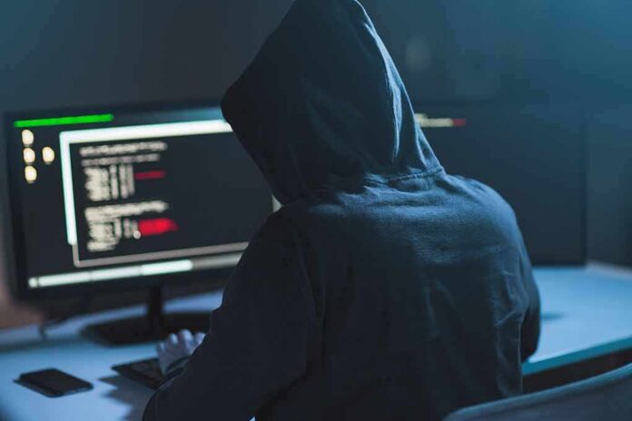 shutterstock_1083511010 Person in hoodie at dual monitors with code