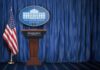 Columbus Day Shock: Press Room Reset White House press briefing podium with U.S. flag and blue curtain