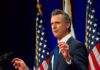 Gavin Newsom speaking at a podium with American flags in the background