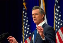 Gavin Newsom speaking at a podium with American flags in the background