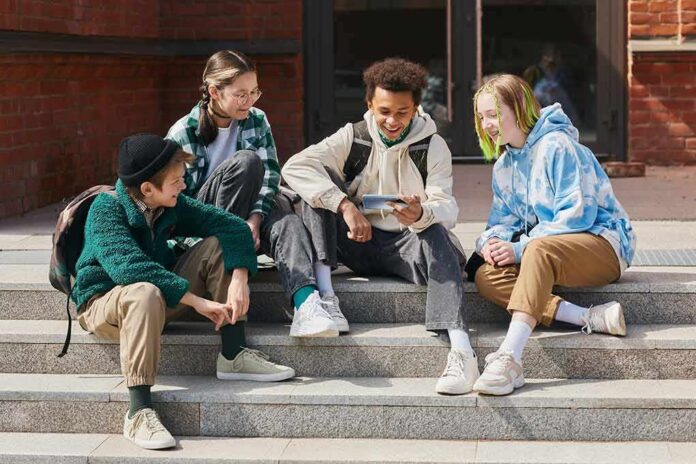 shutterstock_2169268279 Group of teenagers sitting on outdoor steps looking at a smartphone