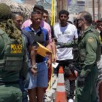 U.S. border patrol officers speak with a line of civilians outdoors