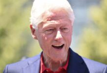 Bill Clinton smiling outdoors in a blue blazer and red shirt